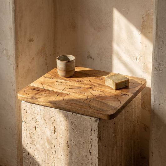 Mango Wood Cheese Platter with food items displayed, set against a rustic wall backdrop and sitting on a concrete pillar.