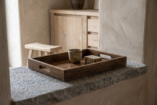 Rectangular wooden tray with rounded corners, dark brown finish, holding ceramic cup and soap on stone window ledge.