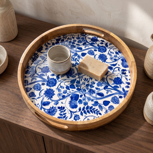 A round wooden serving tray with blue and white floral pattern, placed on a wooden surface with a vase and small bowl nearby.