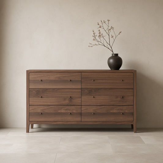 Simple wooden dresser with six drawers, natural finish, dark brown color, displayed against a plain wall with a vase of branches on top of it,