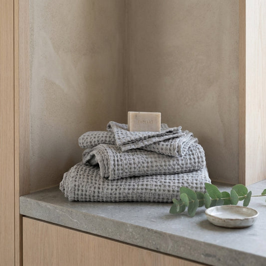 Folded gray towels with honeycomb texture on a countertop with soap bar, leaf, and bowl.