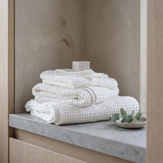Stack of white textured towels on a stone counter with leaves in a minimalist setting.