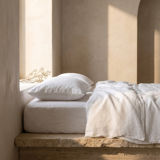 White linen pillowcase on a stone bench against a neutral wall with soft sunlight and shadows
