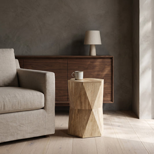 A wooden side table with geometric patterns sits beside a beige armchair, with a cream lamp on a sideboard in the background.