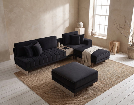 A black sectional sofa and ottoman with a natural wood leg setting on a jute rug in a clean, minimalistic living space with a soft, earthy palette and a large window. No additional technology.