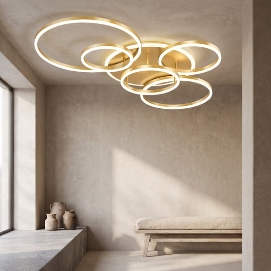 Five circular gold rings lit ceiling lamp, beige walls, windows with light, wooden bench in minimalistic interior