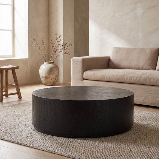 A dark round coffee table on a textured rug, beige sofa, wooden bench and vase in the background, neutral tones, room with natural light,