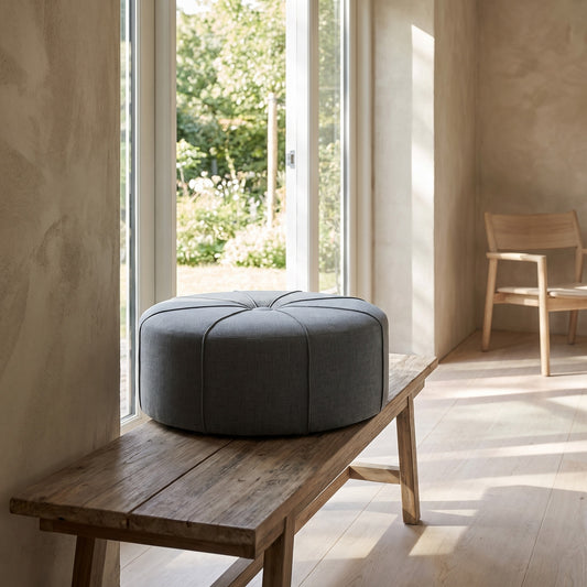 Circular gray ottoman on wooden bench in minimalist room with natural light