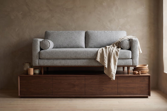 A minimalist 72" sofa in light gray fabric, placed on a wooden platform with bowls and a cloth draped over one end.