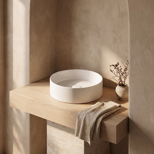 A white round ceramic sink on a wooden ledge in a minimalistic setting.
