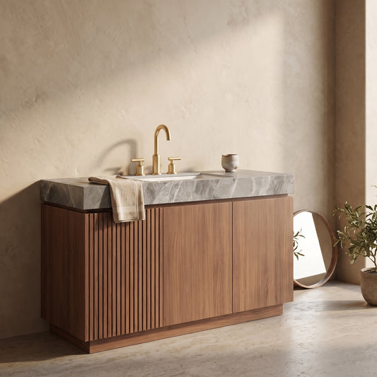 Bathroom vanity set with a marble countertop and brass faucet, placed on a wooden cabinet in a modern setting with a wall mirror and potted plant nearby.