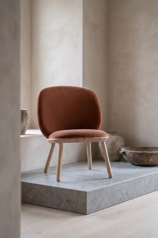 Naive Low Chair with a brown cushion and wooden legs on a marble pedestal, surrounding minimal decor