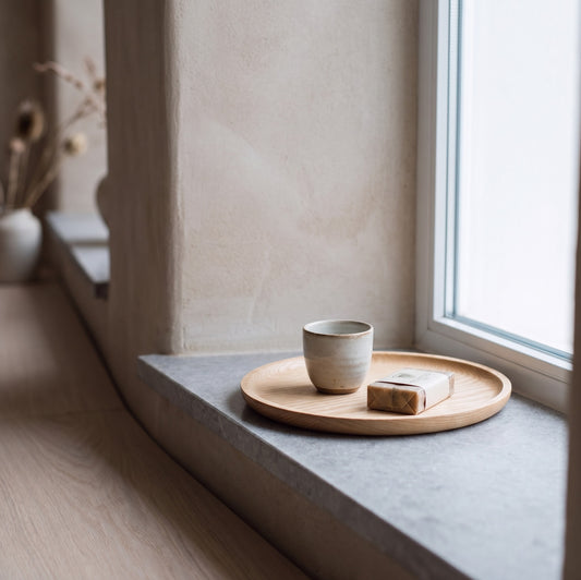 Natural wood round serving tray on windowsill with ceramic cup and soap bar.