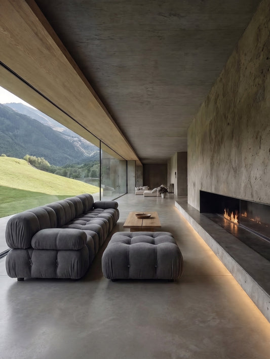 Modular grey linen sectional sofa with tufted cushions and ottoman in a spacious room with concrete floor and fireplace, mountain view outside.