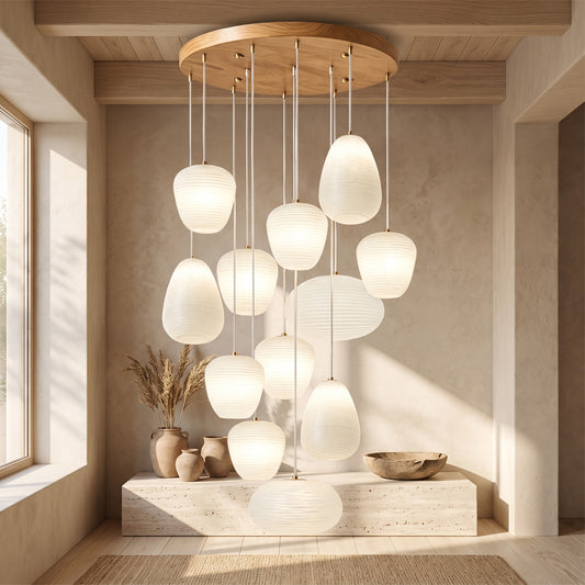 Multi-tiered pendant lights with white ribbed shades hanging from a wooden ceiling fixture in a room with neutral walls and a window.