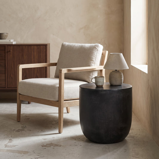Outdoor Lightweight Concrete End Table, Matte Black finish, natural texture, placed in a minimalist room with a linen armchair