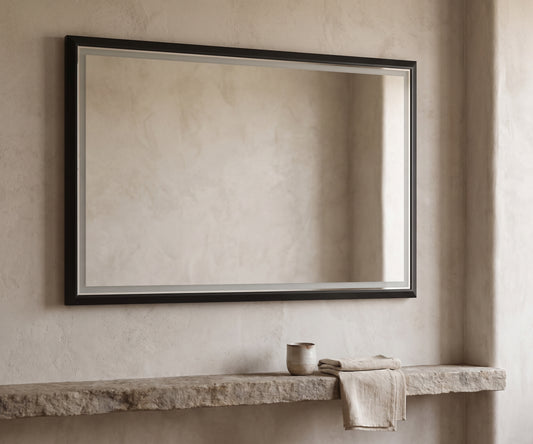 Oversized rectangular mirror with a dark wooden frame and metal detailing, hanging above a rough stone shelf with a beige towel.