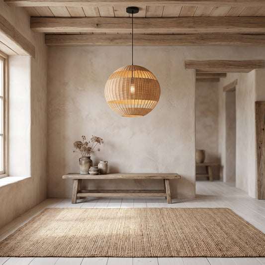 A rustic room with a Palma Wicker Rattan Ball Pendant Light hanging above a bench with vases. Beige walls and wooden beams, natural light from a window, and a woven rug on a light wooden floor.