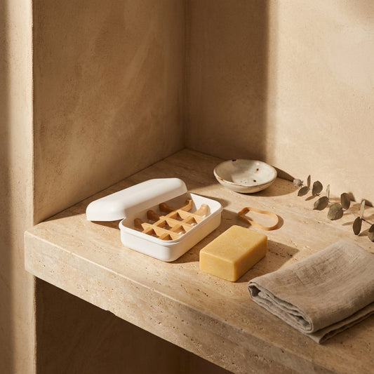 White travel soap keeper with wooden grid, yellow soap bar, beige towel, wabi-sabi bowl on stone ledge