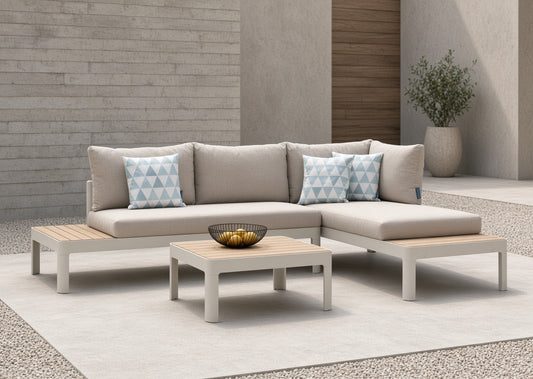 Teak and aluminum modular sofa set with beige cushions and light wood accents, displayed on a light rug with two small blue-patterned pillows and a bowl on a coffee table, against a modern wall background.