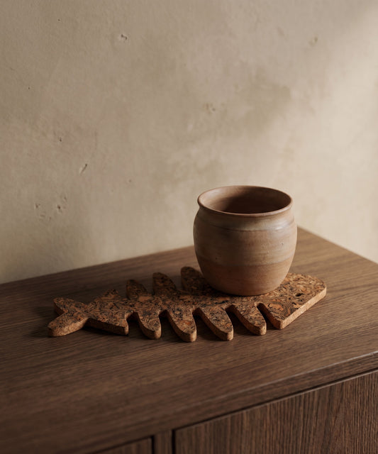 A ceramic cup and a cork trivet placed on a wooden surface against a textured wall