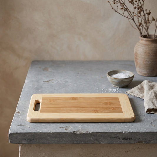 Wooden cutting board with natural finish placed on a stone surface, next to a pottery vase and a bowl of salt with a cloth napkin