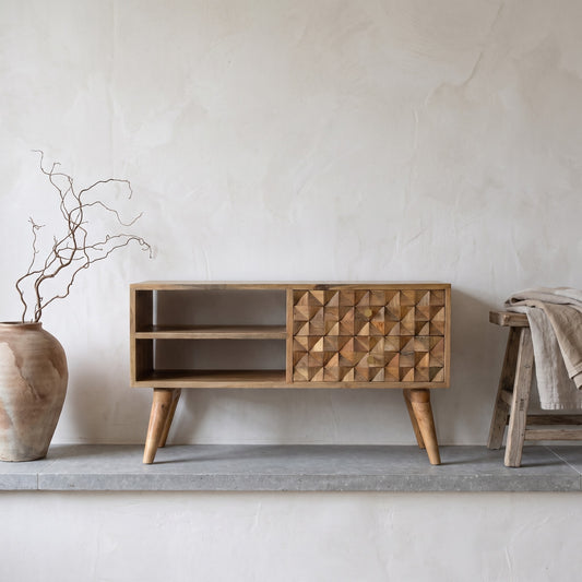 A wooden media unit with carved diamond pattern, natural finish, placed on a concrete surface with a beige wall background.