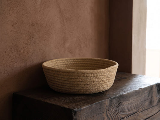 Natural jute-wicker basket placed on dark wooden surface with terracotta wall in background.