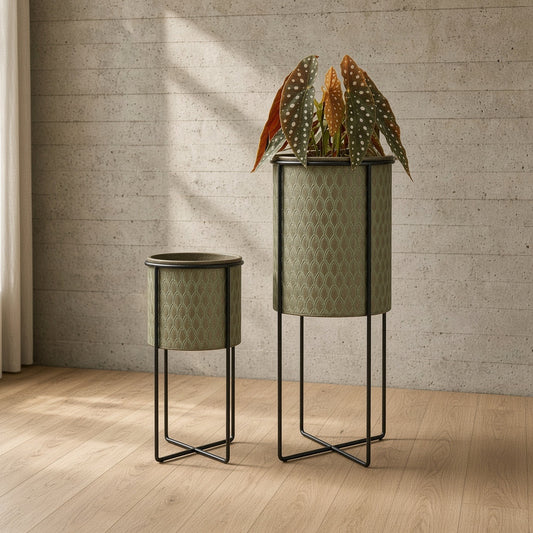 Two textured green plant pots with one containing a plant on decorative stands.