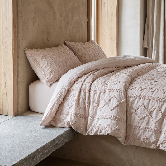 A tufted duvet set in beige, on a white bed against a textured wall, with a window in the background.
