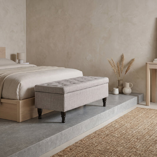Light grey tufted storage ottoman Bench with wooden legs in a modern bedroom setting with neutral tones and minimal decor.