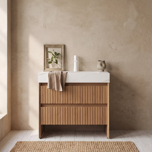 Bathroom vanity and sink with calacatta gold marble top, wooden cabinet with striped drawer, framed plant, candle, and decorative vase against a textured wall.