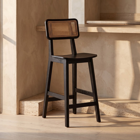 A black cane back wood counter stool on a light wooden floor with a light wall and counter in the background.