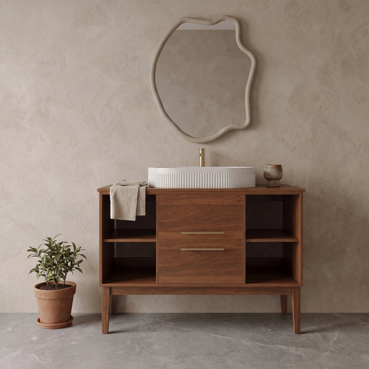 Wooden wall-mounted bathroom vanity with white ceramic sink, beige mirror with irregular edges, neutral-colored wall and floor with potted plant.