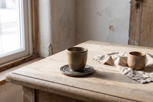 A rustic wooden table with a ceramic drink coaster and cups. The coaster has a Starry Night design.
