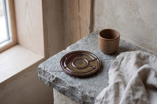 A rock with a drink coaster and small cup, set in a room with wood walls and a window.