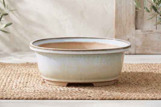 A light blue oval ceramic bonsai pot sitting on a woven mat.