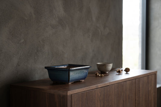 Rectangle-shaped ceramic pot on a wooden surface in a minimalist setting with a rough-textured wall and soft lighting;