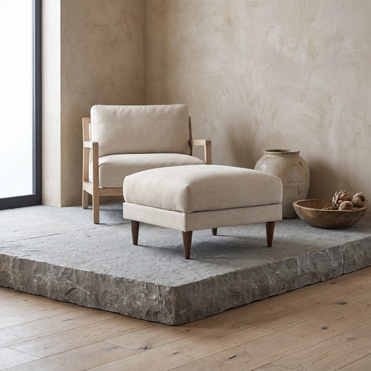 A white down-filled sofa with wooden legs positioned on a floating stone platform with a wooden chair and decorative items in the background.
