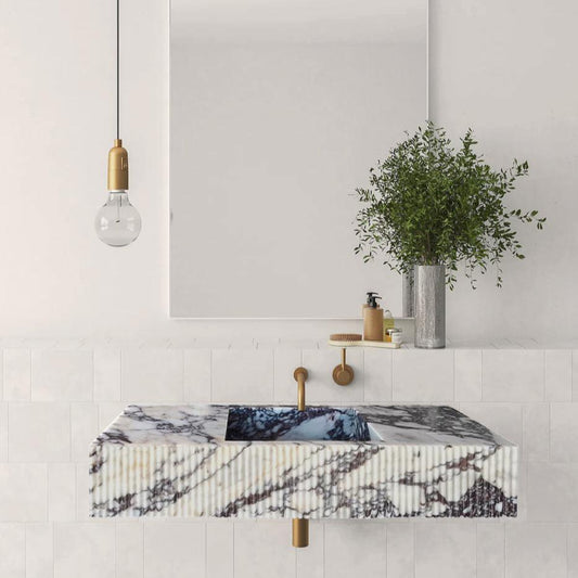 Marble sink with fluted edges in Calacatta Viola on wall-mounted vanity, brass fixtures, white tiled backsplash. No text overlay or issues.