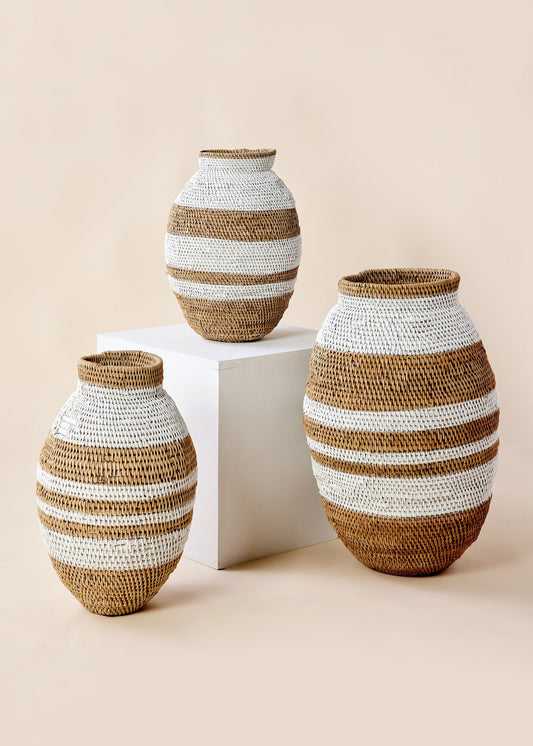 Three rattan baskets with white stripes in varying sizes on a neutral background.